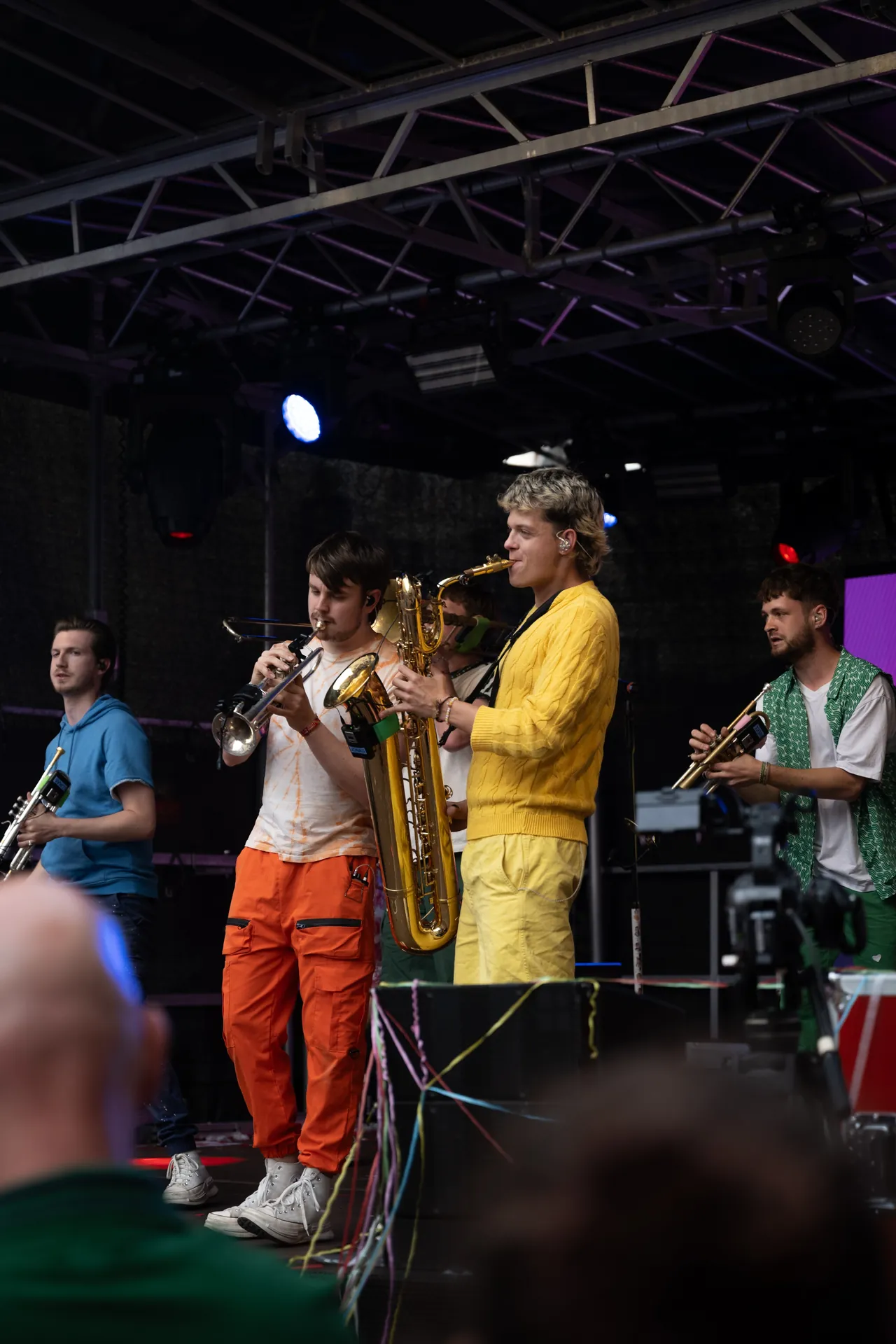 Fünf Musiker spielen auf einer Bühne Trompete und Saxophon, ein Zuschauer ist im Vordergrund zu sehen.