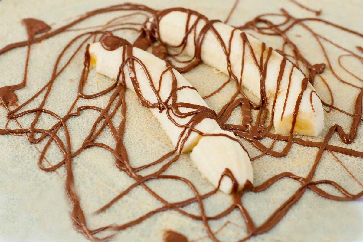 Ein appetitlicher Crepe wird mit Bananenstucken belegt und mit flussiger Schokolade verziert.