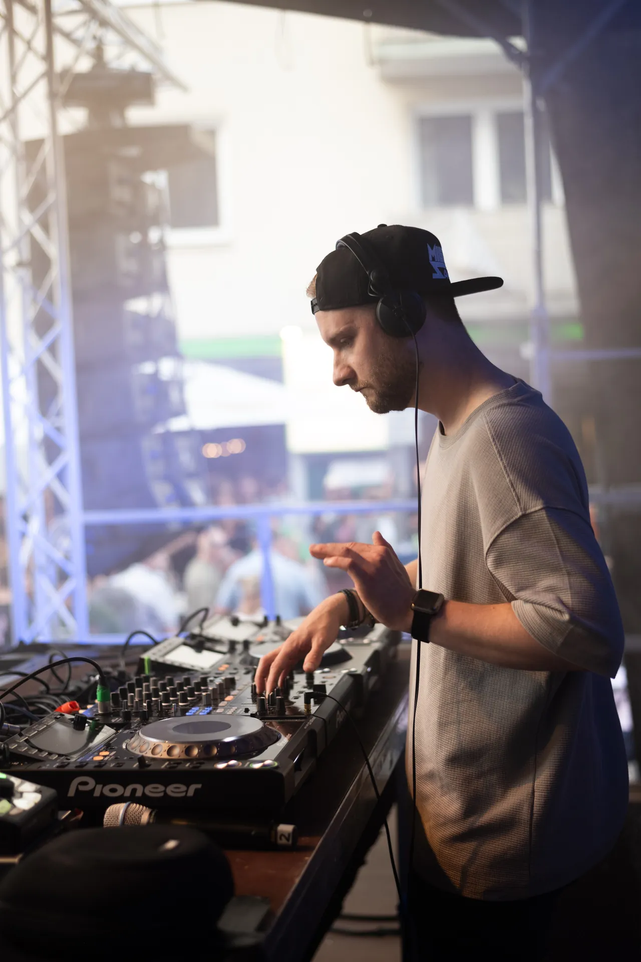 Ein DJ mit Kopfhörern und schwarzer Kappe legt Musik an einem Pioneer Mischpult auf.