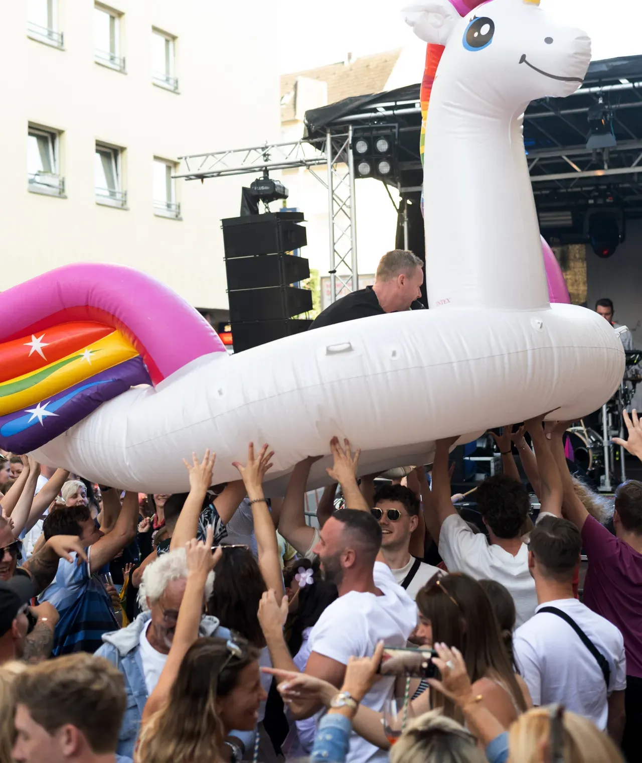 Besucher halten ein aufblasbares Einhorn in die Höhe, ein Mann steht darauf, im Hintergrund eine Bühne.