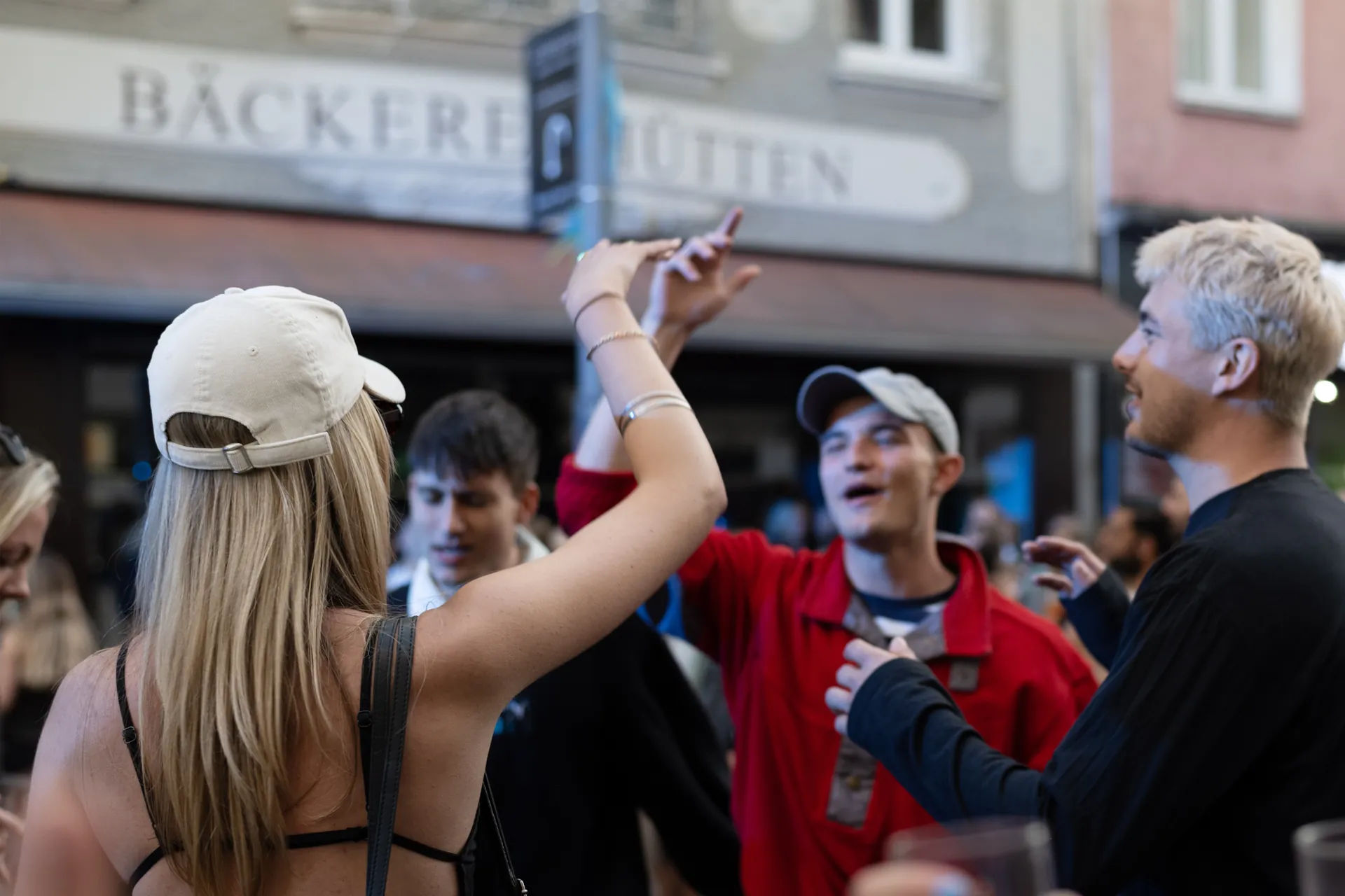 Mehrere junge Menschen stehen im Freien zusammen und unterhalten sich gestenreich.