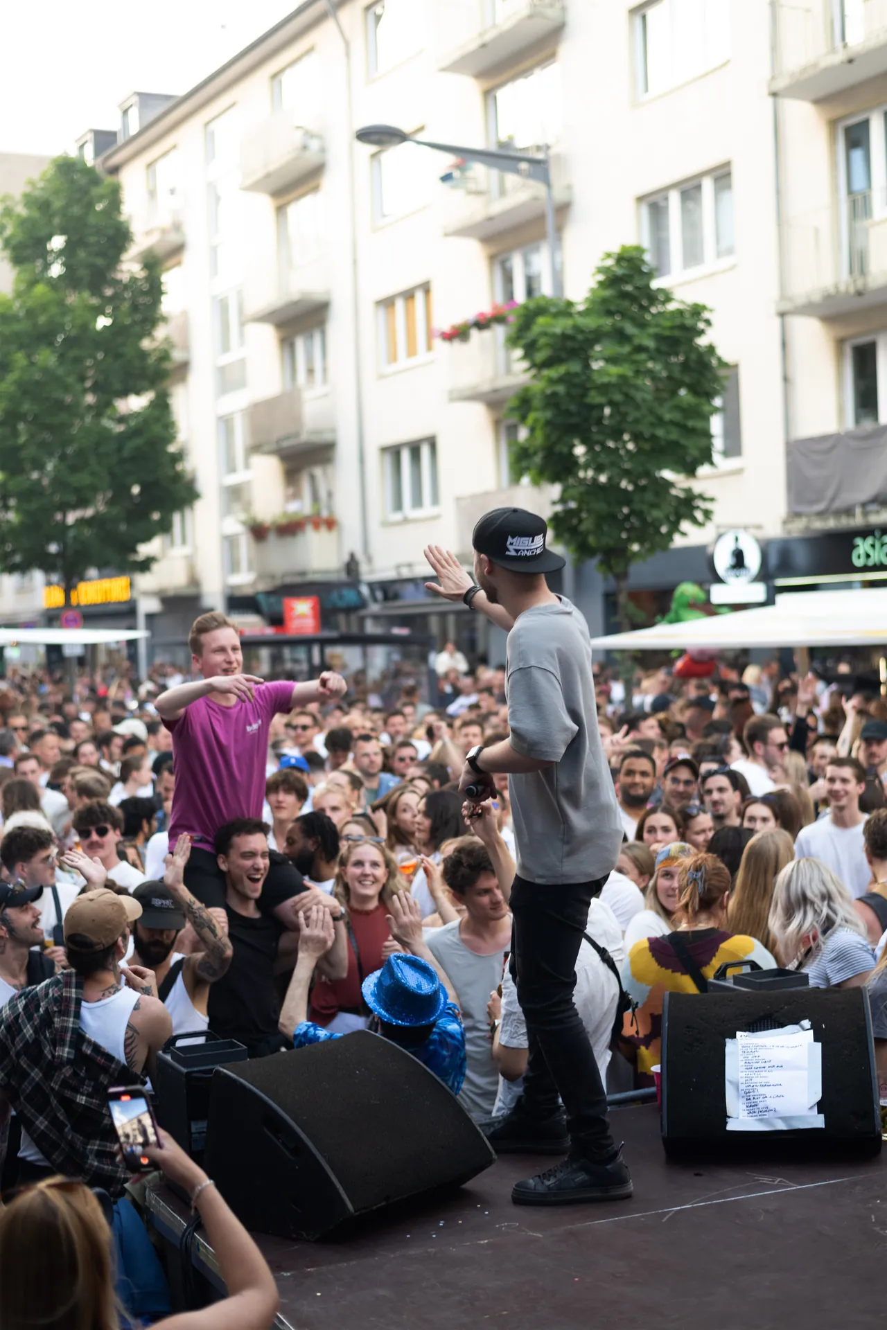 Ein Musiker steht auf der Bühne und animiert eine große Menschenmenge zum Mitfeiern.