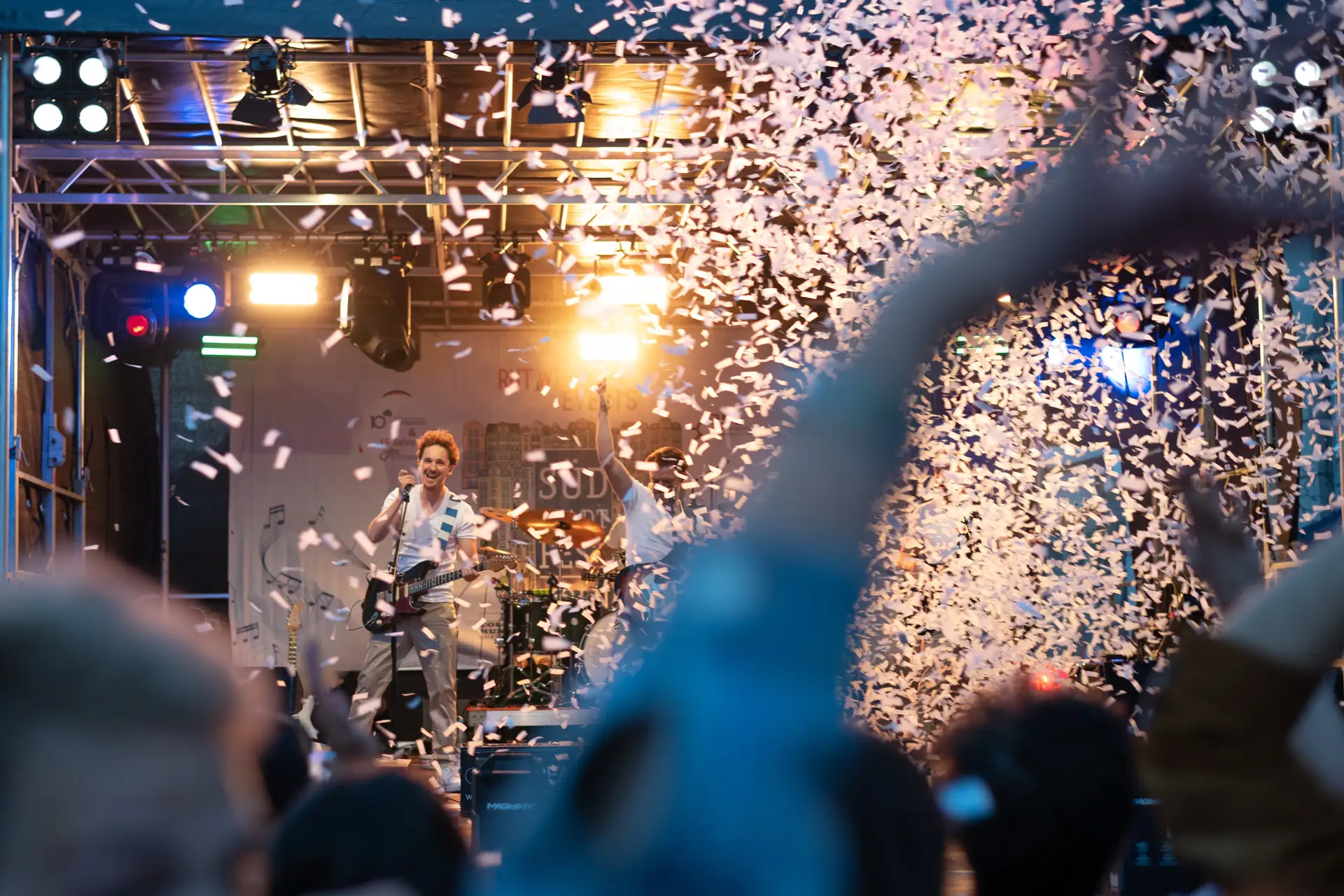 Auf dem Sudstadtfest spielt eine Band auf der Buhne, wahrend Konfetti in der Luft wirbelt und Besucher jubeln.