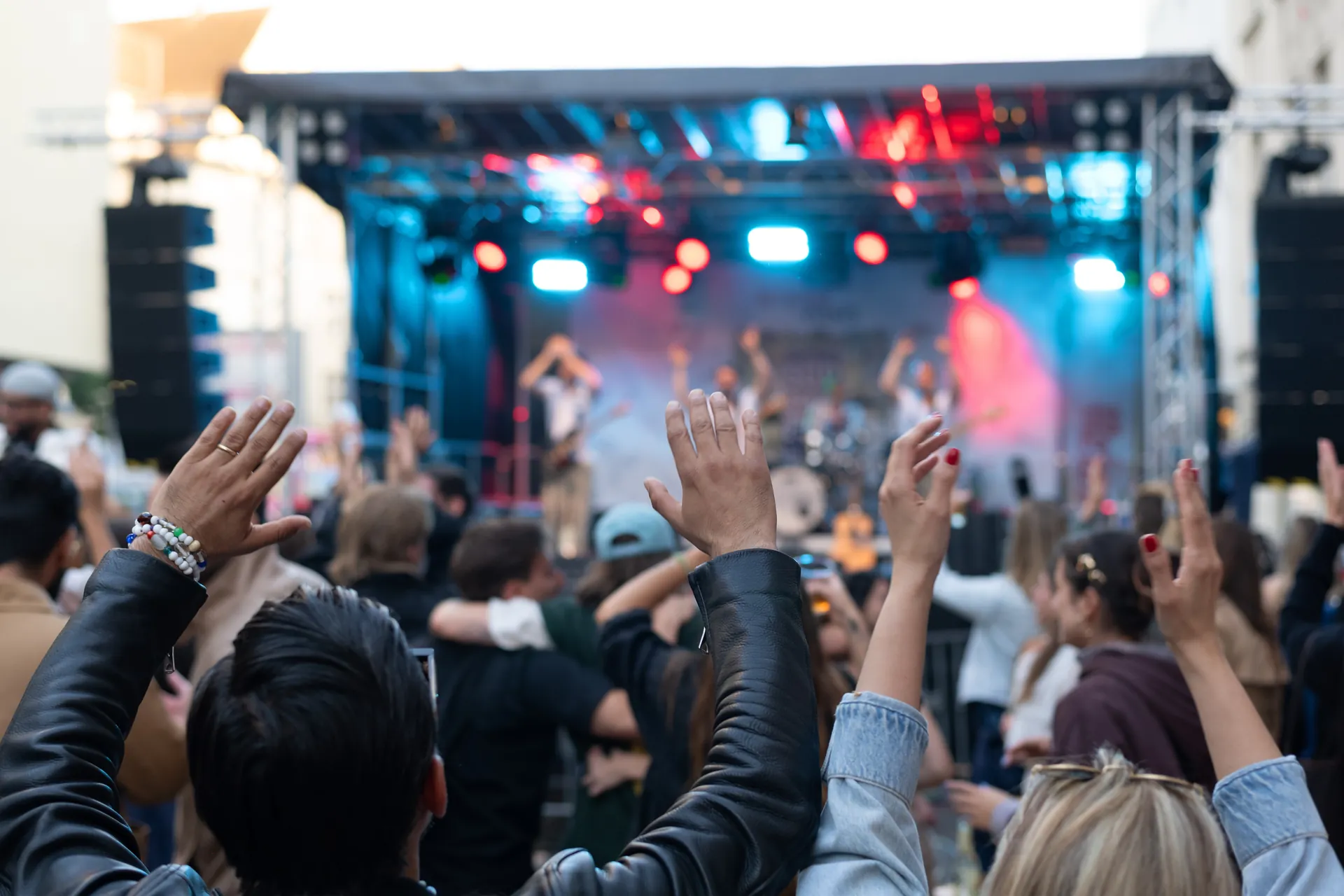 Besucher feiern mit erhobenen Handen vor einer Buhne mit Musikern und roter und blauer Beleuchtung.