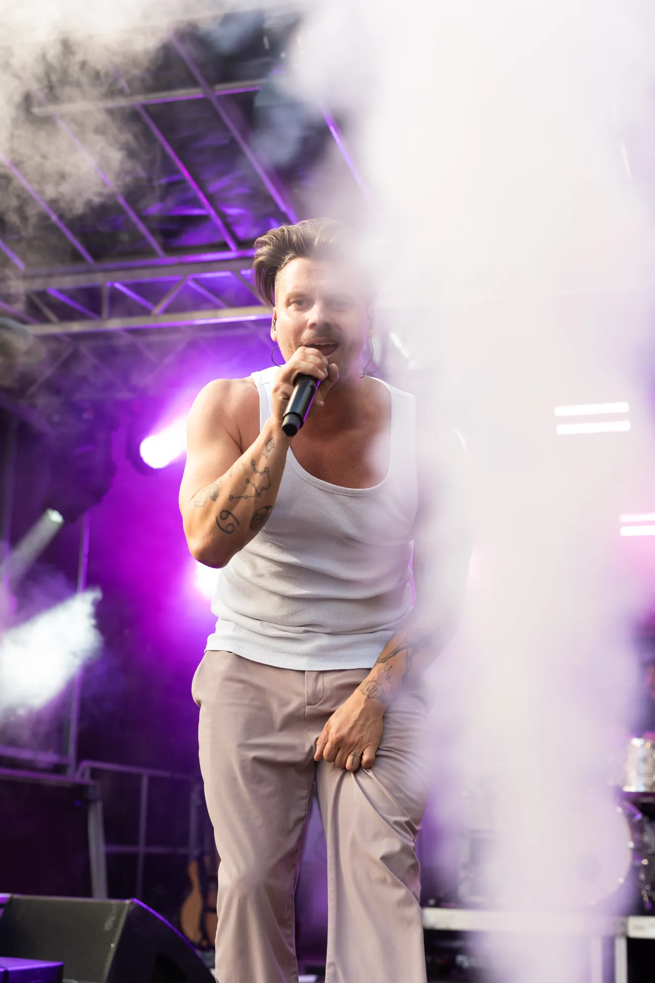 Ein Mann mit Tattoos singt mit einem Mikrofon auf einer Bühne mit lila Licht.