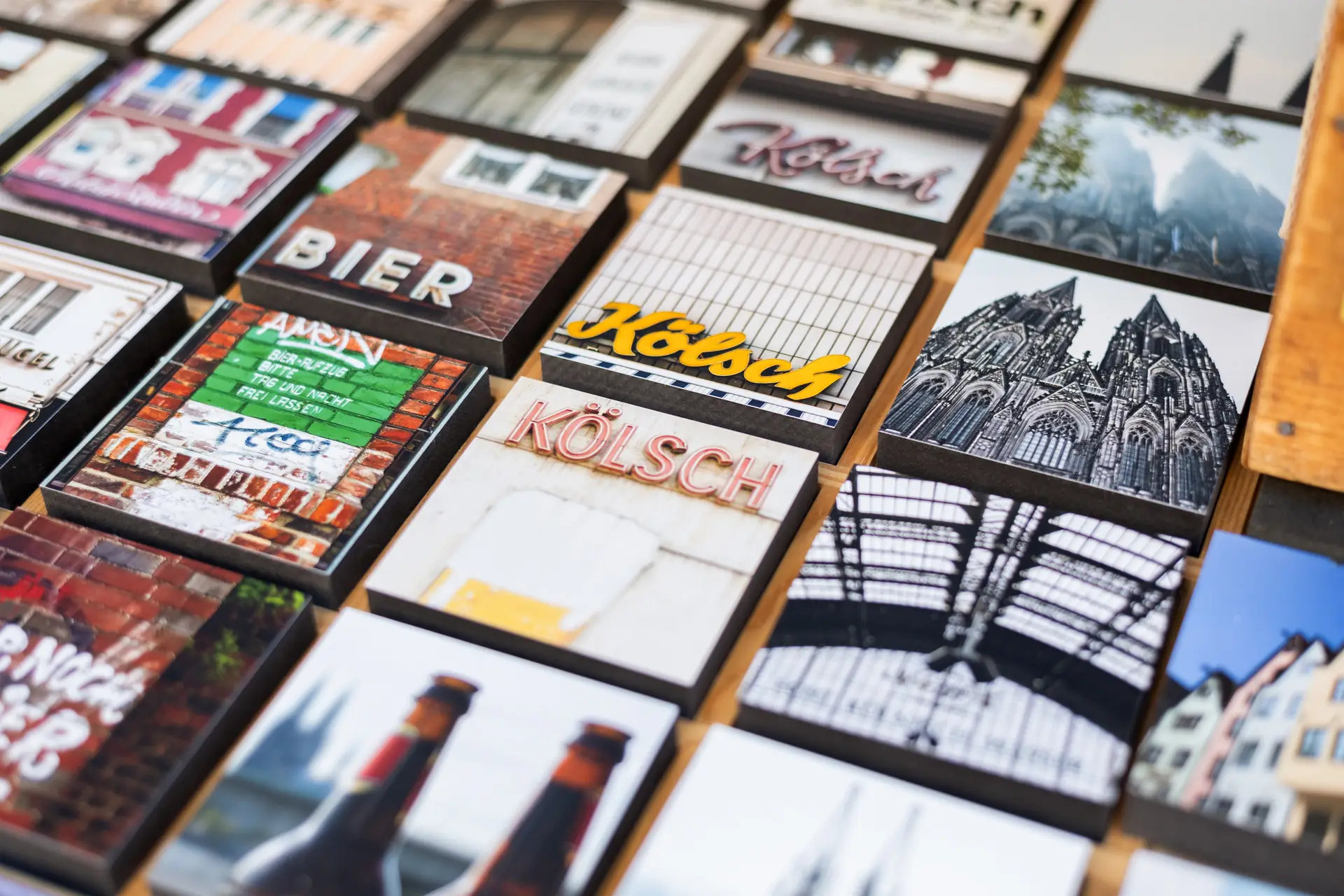 Eine Nahaufnahme zeigt viele Souvenir-Magnete mit Koln-Motiven auf einem Verkaufstisch, darunter Bierwerbung, der Dom und Gebaude.