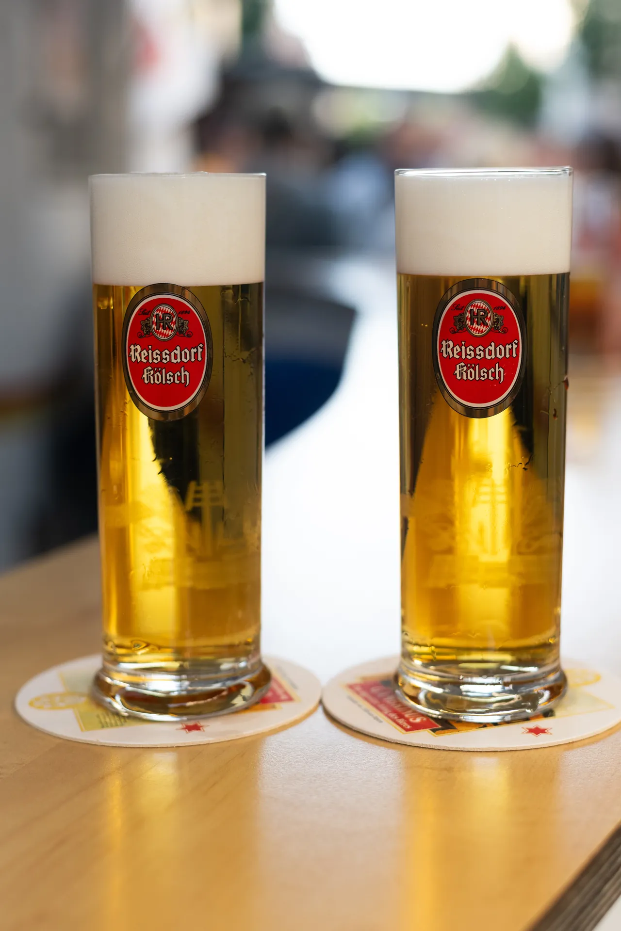 Zwei Glaser Reissdorf Kolsch stehen auf einem Tisch, die Etiketten mit dem bekannten Logo sind gut sichtbar.
