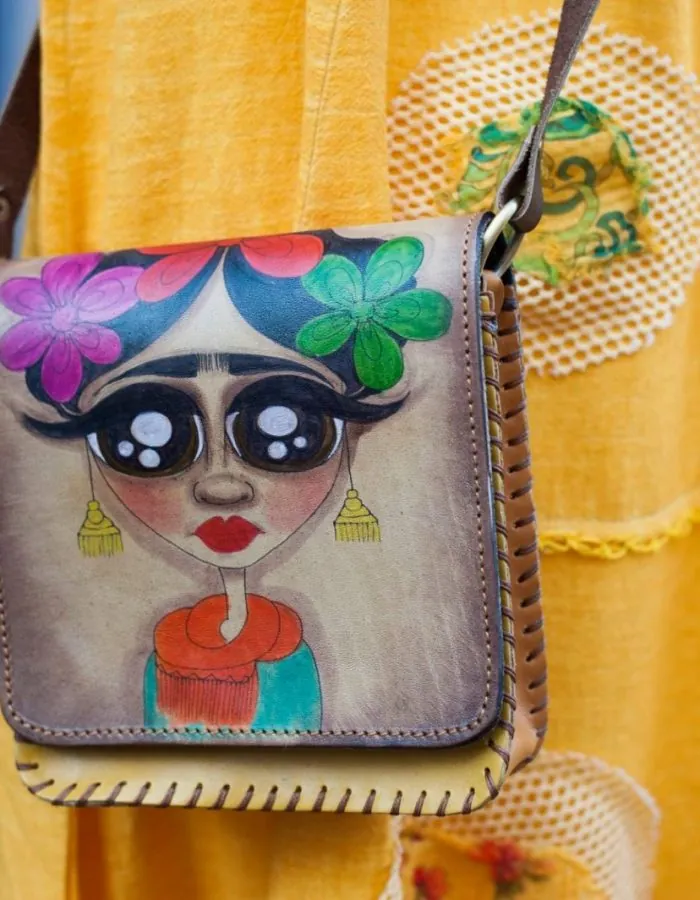 Handbemalte Ledertasche mit buntem Frida-Motiv vor gelbem Stoff
