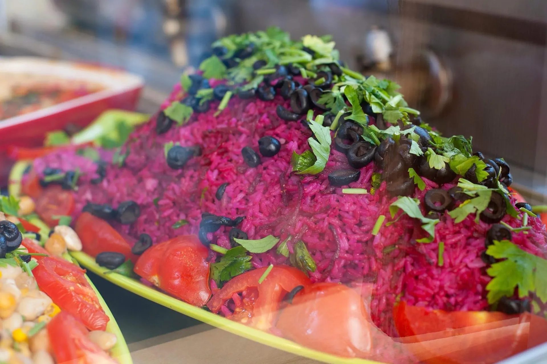 Appetitlicher Beet-Reis-Salat mit Tomaten, Oliven und frischen Kräutern auf gelbem Teller