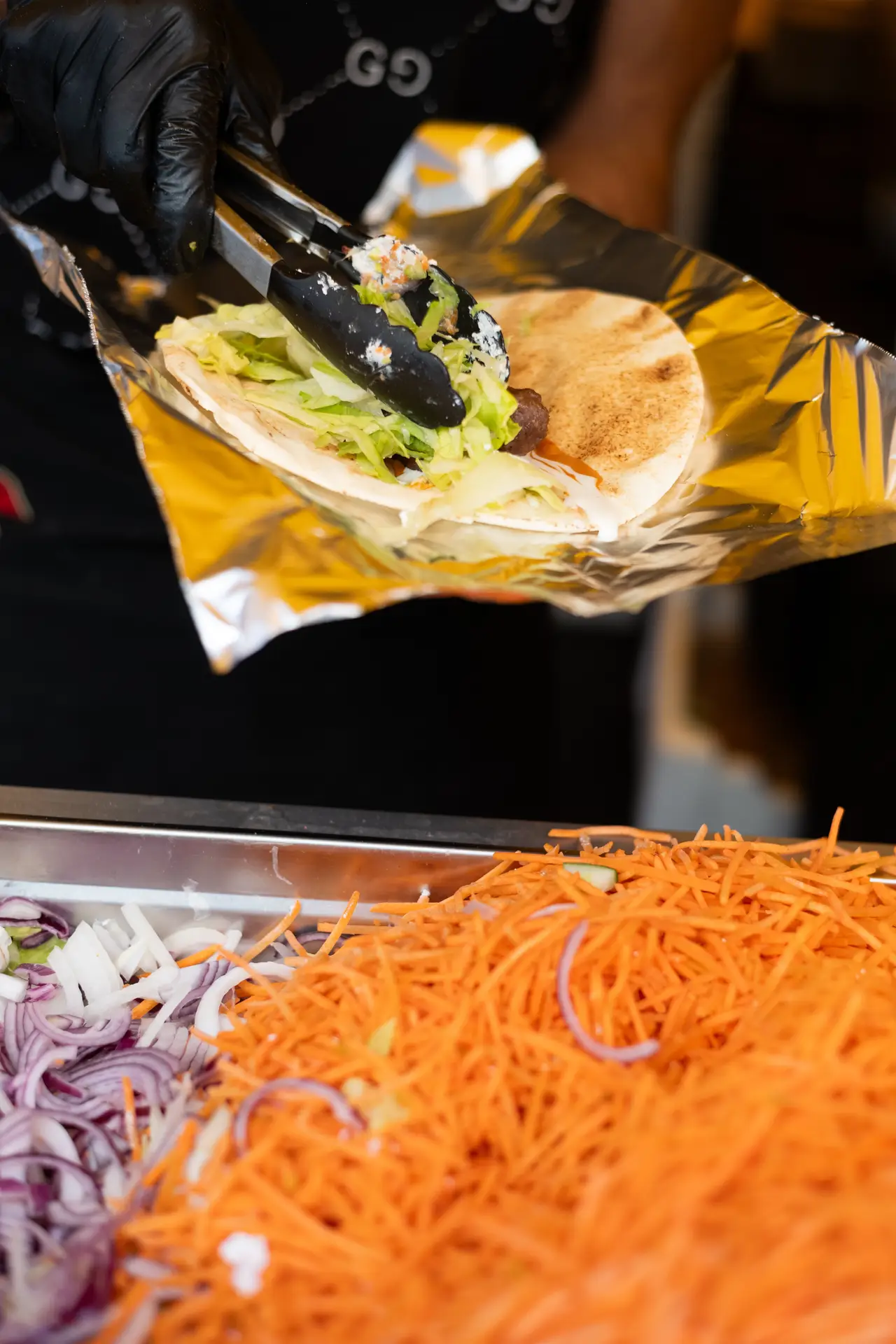 Eine Person mit schwarzen Handschuhen befüllt einen Wrap mit Salat und Sauce