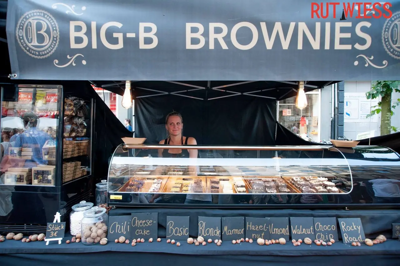 Freundliche Verkäuferin präsentiert eine Auswahl an köstlichen Brownies auf einem Marktstand