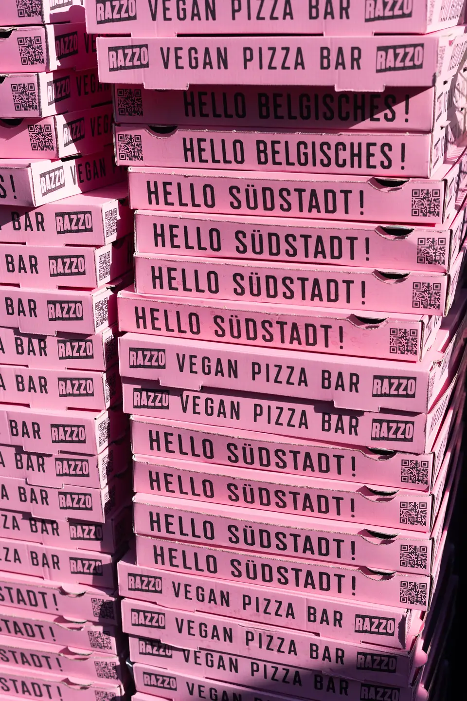 Stapel rosafarbener Pizzakartons mit der Aufschrift RAZZO Vegan Pizza Bar
